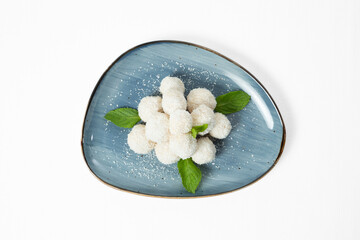 Homemade coconut balls covered in shredded coconut, decorated with mint leaves, served on a plate. Isolated on white background