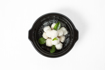 Homemade coconut balls covered in shredded coconut, decorated with mint leaves, served on a plate. Isolated on white background