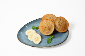 Homemade banana muffins with fresh banana slices and mint leaves, served on a plate. Isolated on white background