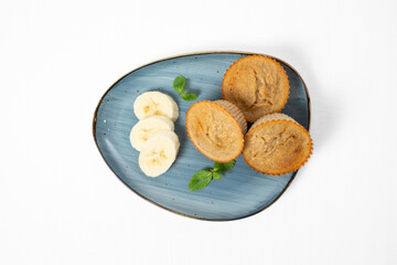 Homemade banana muffins with fresh banana slices and mint leaves, served on a plate. Isolated on white background