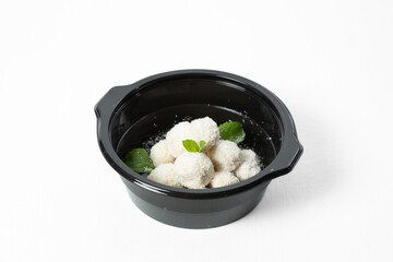 Homemade coconut balls covered in shredded coconut, decorated with mint leaves, served on a plate. Isolated on white background