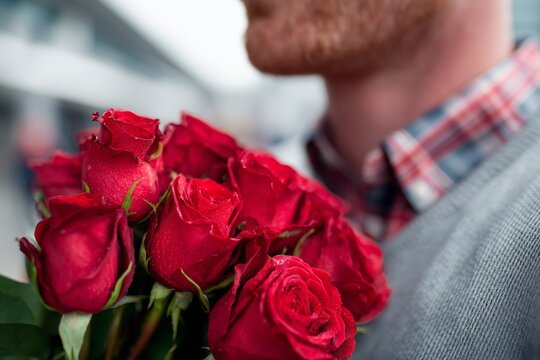 Man holding a fresh bouquet of red roses with visible water droplets, expressing romantic gesture and affection - Powered by Adobe