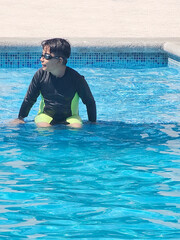 Latino boy plays in the pool alone during his vacation or weekend wearing a swimsuit to protect himself from the sun