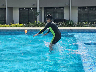 Latino boy plays in the pool alone during his vacation or weekend wearing a swimsuit to protect himself from the sun