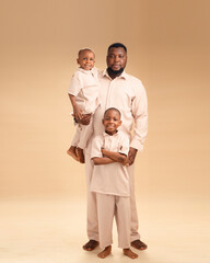 In a moment of quiet pride, an African father holds his youngest while the elder stands tall beside...