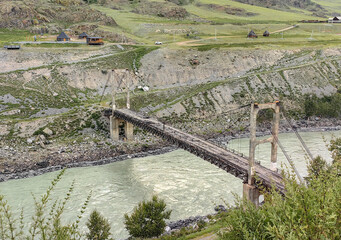 A picturesque suspension bridge stretches across a flowing river, embraced by nature's beauty.