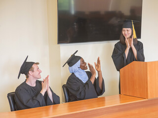 A young woman stands at the lectern and delivers a graduation speech to her classmates. 