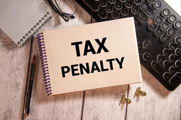 TAX PENALTY text on a notebook with pen on wooden background.