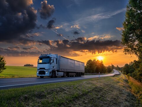 White truck driving on the asphalt road in rural landscape at sunset