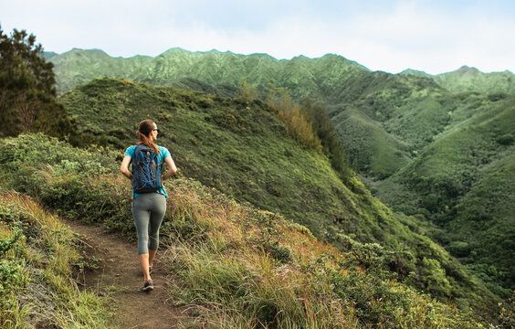 Tourist female hiking enjoying breathtaking view of Hawaiian mountains covered by green lush vegetation
