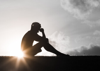 Sad and lonely man silhouette sitting in the park head down 