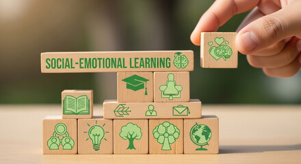 Hand placing a wooden block with social emotional learning icons on a stack of similar blocks