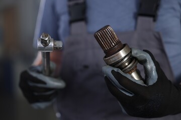 Auto part. Professional mechanic with drive shaft and tool indoors, closeup
