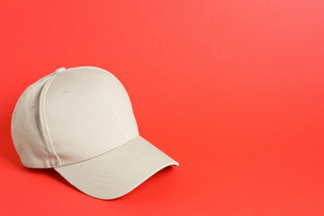 Beige baseball hat on coral background, space for text