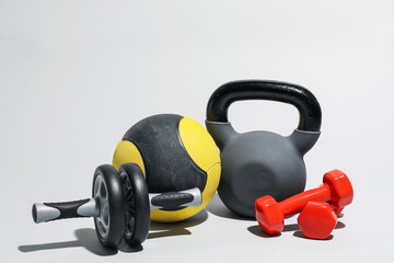 Medicine ball, ab wheel, kettlebell and dumbbells on light grey background