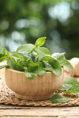 Mortar with fresh mint leaves on wooden table against blurred green background, closeup