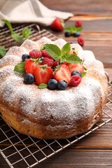 Tasty Bundt cake with powdered sugar and berries on wooden table, closeup