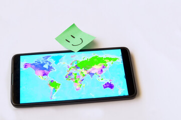 Mobile phone with a world map on the screen and a green note with a smiley face