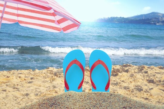 Pink flip flops resting on the beach with a clear blue sky and ocean waves in the background. summer time and season, sea, sand, summer items, seaside, concept 
