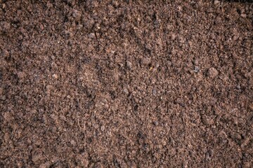 Detailed close-up view of a dirt surface, highlighting the rich brown tones and granular texture of the soil. brown soil, background, earth, agriculture, nature