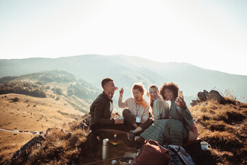 Friends drinking coffee and taking selfie on mountain hike at sunrise