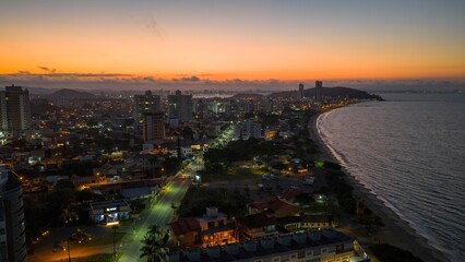 Fototapeta premium Aerial view of Penha coastline at sunset with city lights and calm ocean waters.
