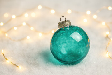 Beautiful turquoise color transparent glass christmas ball on a snow with tiny warm christmas lights
