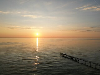 Serene Sunset over the Sea: The sun dips towards the horizon, painting the ocean with hues of orange and gold, while a distant pier stretches into the tranquil water.