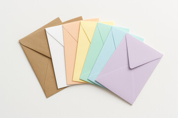 Set of assorted pastel and kraft paper envelopes arranged in a fan shape over minimal white surface, ideal for packaging, letters, or creative stationery visuals