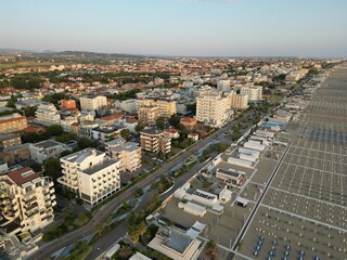 Aerial View of Coastal Cityscape: An expansive aerial view of a bustling coastal city unfolds, showcasing rows of buildings parallel to a scenic beach and sparkling sea.