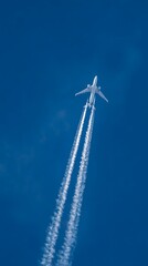 A high-flying airplane leaves dual contrails streaking across a clear, deep blue sky, emphasizing the speed and altitude of modern aviation.