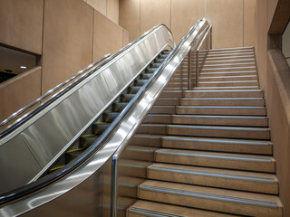 Modern escalator and adjacent staircase inside a building. Concept of accessibility option, urban infrastructure, and pedestrian flow solutions.