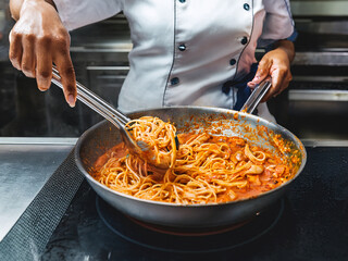 Dynamic Close-up: Chef Tossing Cooked Pasta into Simmering Sauce with Tongs


