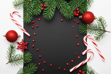 Festive Christmas Decor: Christmas decorations of the season in a flat lay. Featuring fir tree branches, candy canes, baubles and red berries on a black surface.