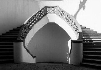Symmetrical double staircase with ornate railing and dramatic shadows on white curved walls.
