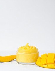 Vibrant mango cream in glass jar with fresh fruit slices on white background, natural cosmetic product