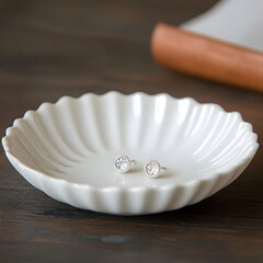 White ceramic dish with fluted edges containing two small earrings on a dark wooden surface.