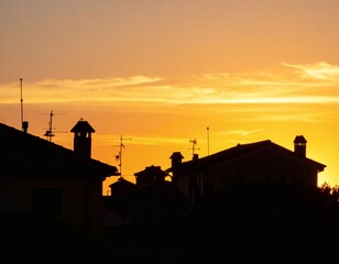 Silhouettes of suburban rooftops with chimneys and antennas against a dramatic golden and orange sunset sky.