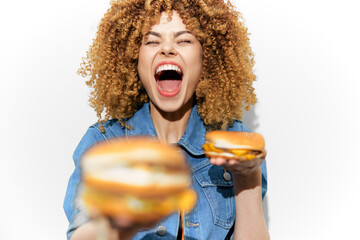 Joyful woman with curly hair enjoying delicious burgers, showcasing excitement and happiness in a bright, cheerful setting with a fun and playful atmosphere