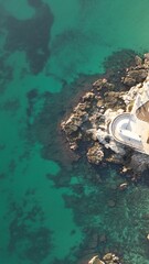 Coastal Lighthouse Amidst Emerald Waters: An aerial panorama captures a sturdy lighthouse, perched upon a rugged, rocky islet, embraced by the stunning embrace of pristine emerald waters.