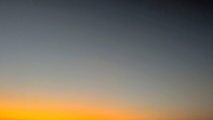 A horizontal gradient sky, transitioning from dark blue to vibrant orange and yellow, with a few subtle stars visible, depicting either dawn.