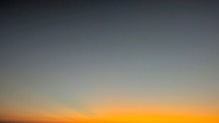 A vibrant gradient sky transitions from dark blue at the top to bright orange and yellow at the bottom, suggesting either dawn with subtle stars visible.