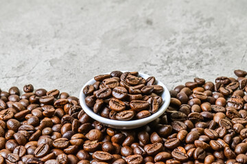 Close up view of roasted coffee beans on the little or small white plate. scattered on grey or gray...