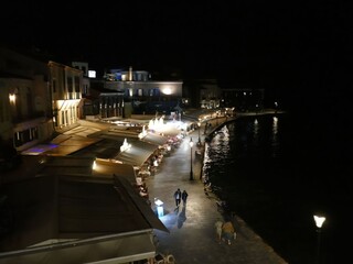 Nighttime view of Venetian harbor waterfront in Chania, Crete, with tourists strolling past glowing...