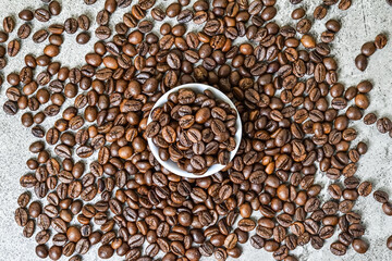 Top view of roasted coffee beans on little or small white plate. scattered on grey or gray cement...