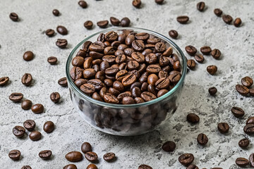 Close up view of roasted coffee beans on the glass bowl. scattered on grey or gray cement as...
