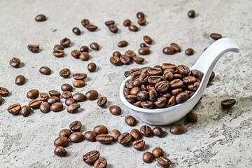 Close up view of roasted coffee beans on the white spoon. scattered on grey or gray cement as...