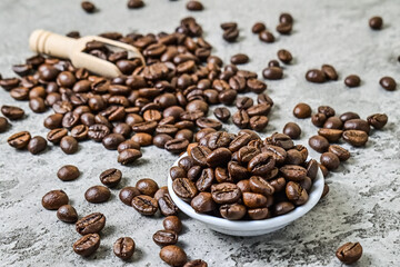 Close up view of roasted coffee beans on the little or small white plate and wooden scoop. scattered on grey or gray cement as background.