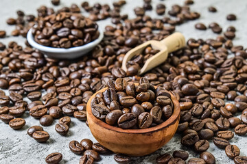 Close up view of roasted coffee beans on the little or small wooden bowl, wooden scoop and white plate. scattered on grey or gray cement as background.