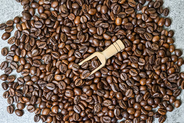 Top view of roasted coffee beans with little or small wooden scoop. scattered on grey or gray...